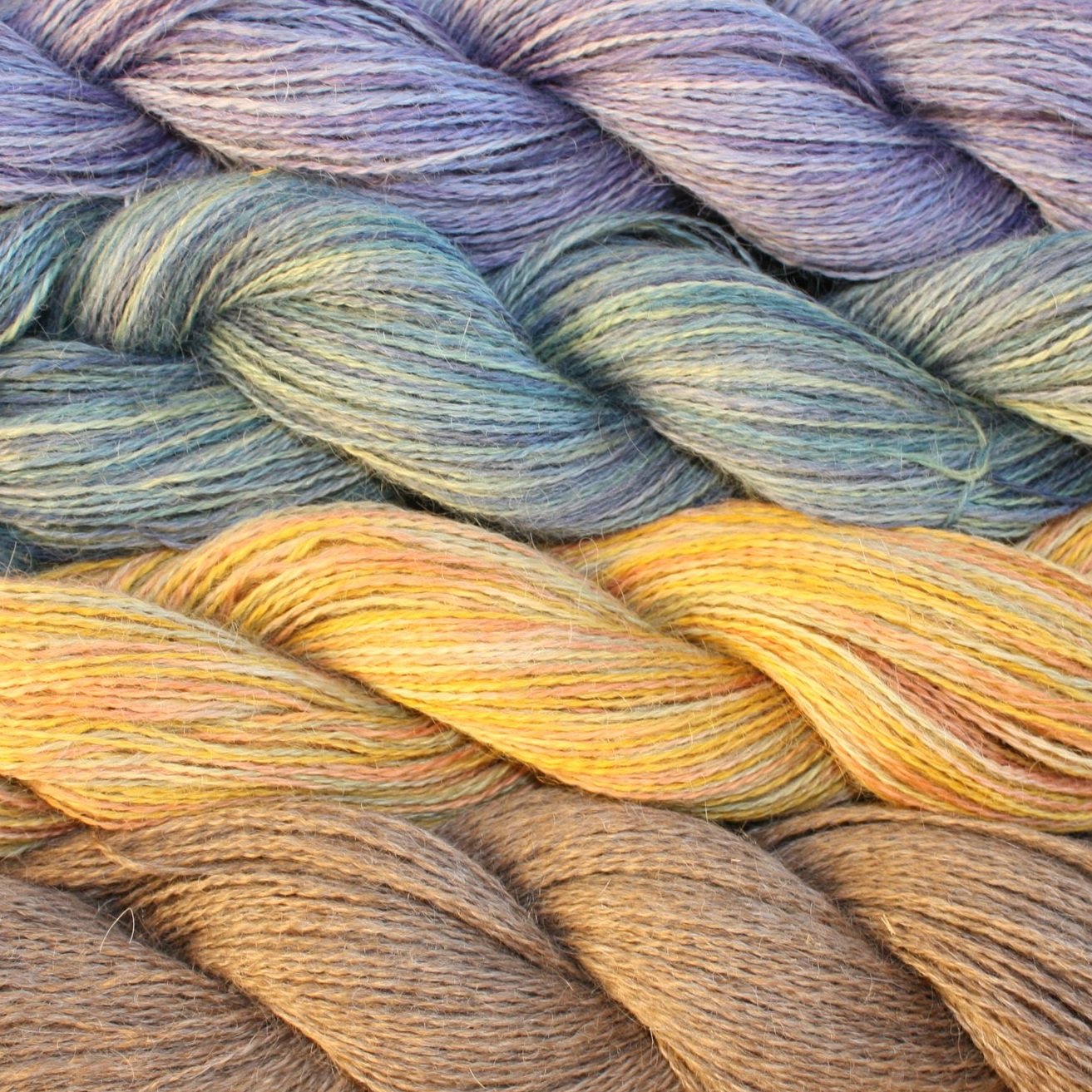 Colorful strands of hand-dyed yarn in shades of purple, green, yellow, and brown, arranged in a braided pattern, showcasing a variety of textures ideal for knitting and crafting projects.